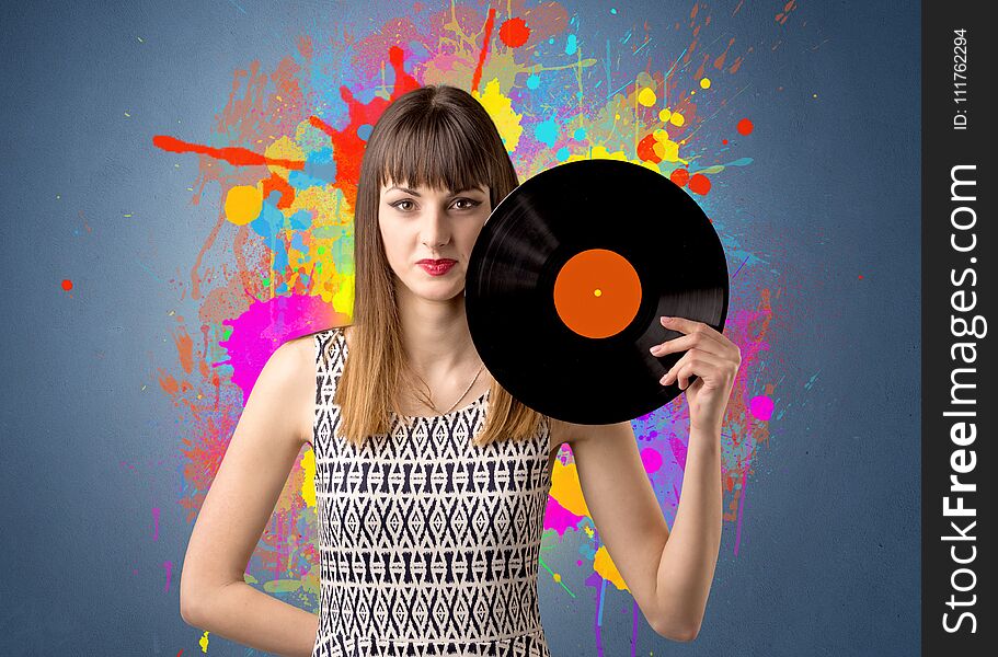 Young lady holding vinyl record on a grey background with colorful splashes behind her