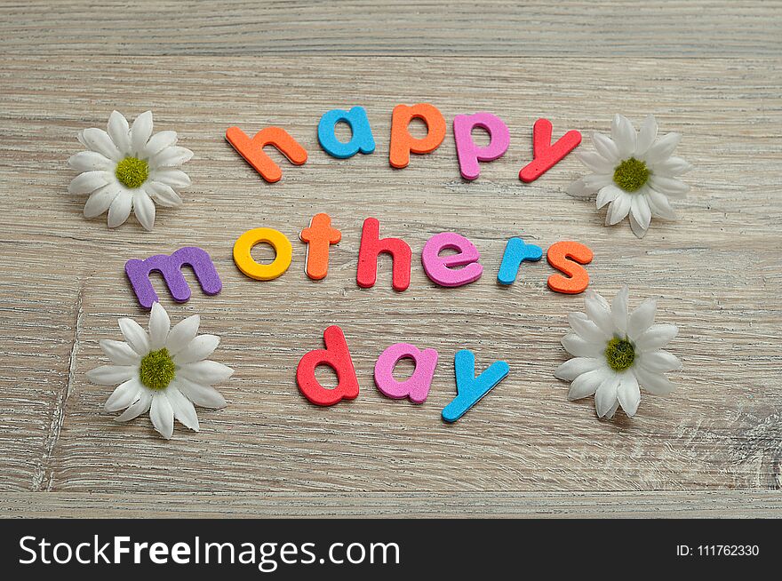 Happy mothers day in colorful letters on a wooden background with white daisies. Happy mothers day in colorful letters on a wooden background with white daisies