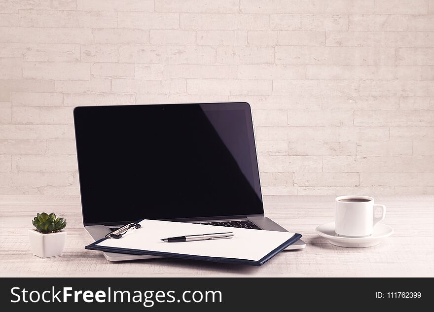 Close up of business office desk with pen board coffee in front of empty white brick textured wall background. Close up of business office desk with pen board coffee in front of empty white brick textured wall background.