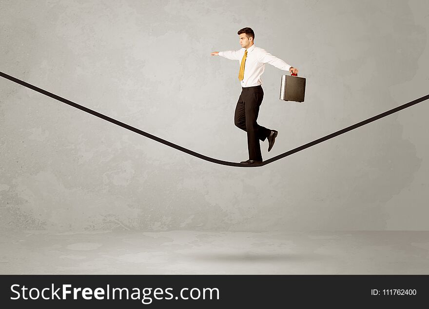 An elegan businessman in suit balancing on a tight rope with a briefcase in front of grey urban wall background environment concept. An elegan businessman in suit balancing on a tight rope with a briefcase in front of grey urban wall background environment concept
