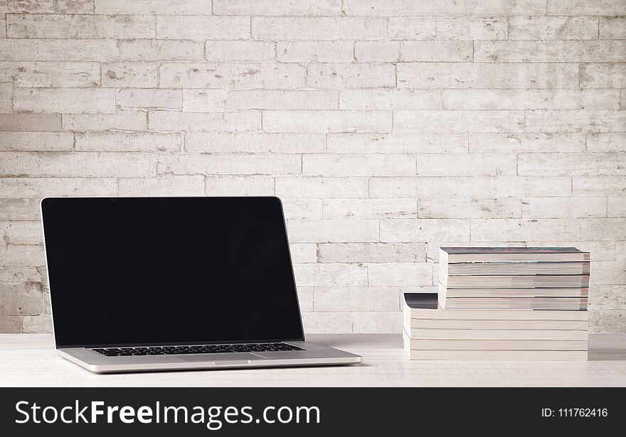 An open laptop on an office desk with flower, coffee, books in front of white brick wall background concept. An open laptop on an office desk with flower, coffee, books in front of white brick wall background concept