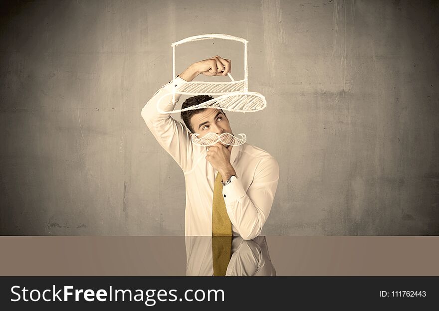 A young happy businessman in elegant suit drawing funny hat and mustache in empty grey space with a chalk illustration concept. A young happy businessman in elegant suit drawing funny hat and mustache in empty grey space with a chalk illustration concept