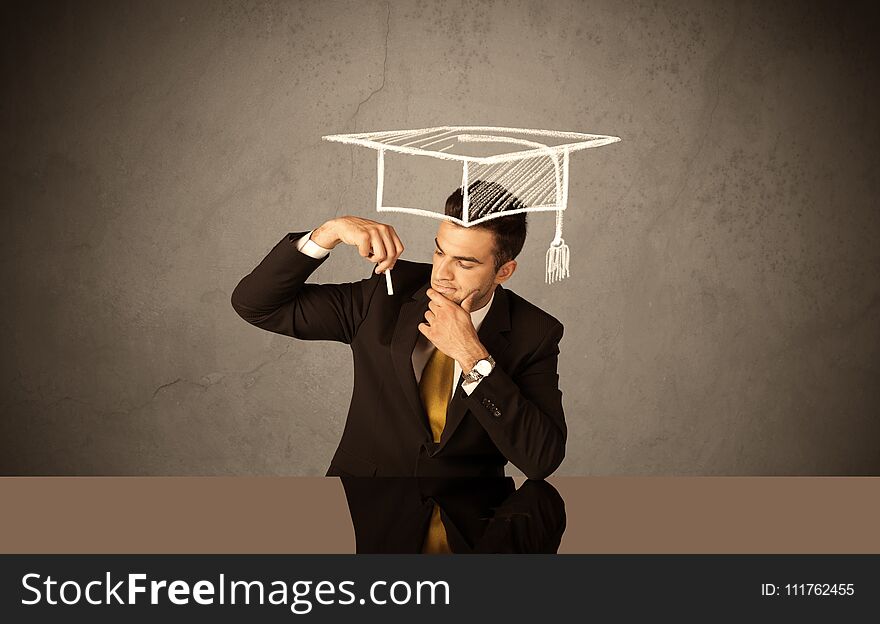 An elegant, successful university student drawing himself a square academic mortarboard cap with a chalk in front of grey wall background concept. An elegant, successful university student drawing himself a square academic mortarboard cap with a chalk in front of grey wall background concept