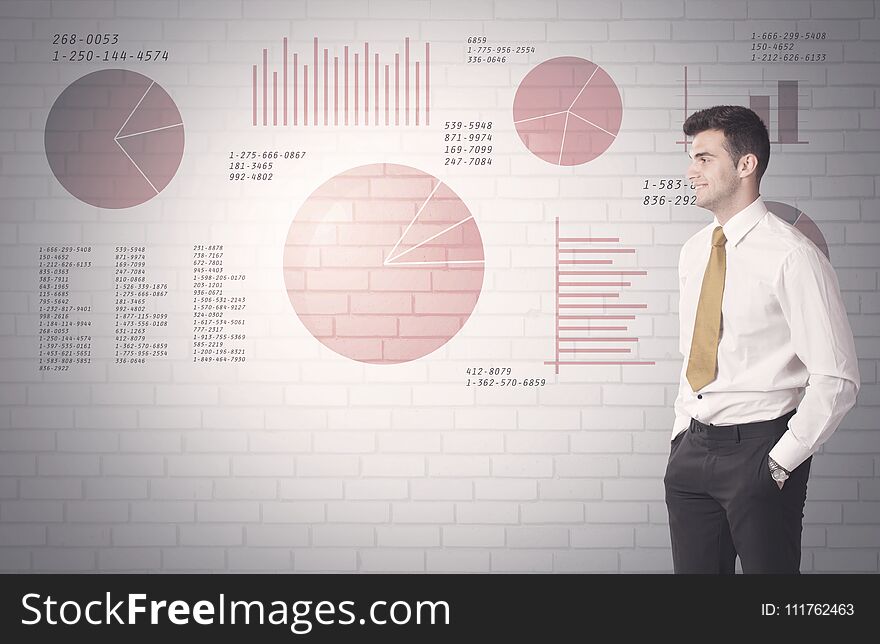 Young sales business male in elegant suit standing in front of brick wall background with lines and pie charts concept. Young sales business male in elegant suit standing in front of brick wall background with lines and pie charts concept