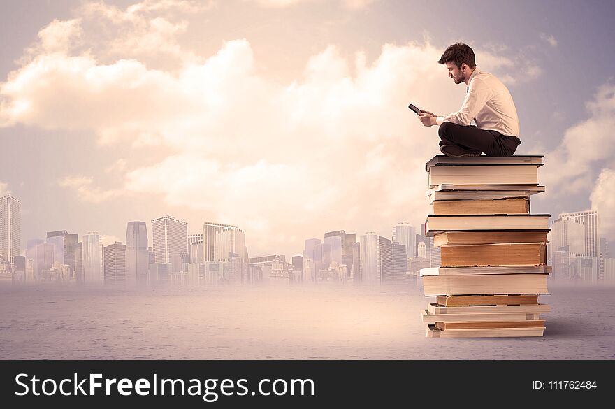 A serious student with laptop tablet in elegant suit sitting on a stack of books in front of cityscape with clouds. A serious student with laptop tablet in elegant suit sitting on a stack of books in front of cityscape with clouds