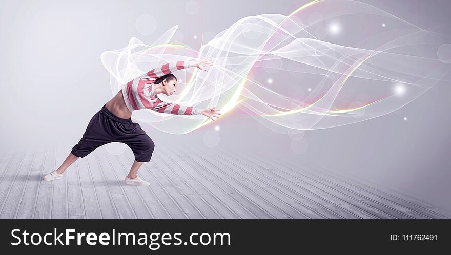 A beautiful young hip hop dancer dancing contemporary urban street dance in front of grey wall background with smokey lines and glitter concept. A beautiful young hip hop dancer dancing contemporary urban street dance in front of grey wall background with smokey lines and glitter concept.