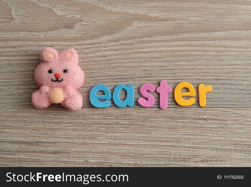 A pink bunny shape marshmallow with the word easter isolated on a wooden background
