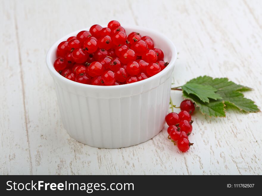 Red currants with leaves in the bowl on wood