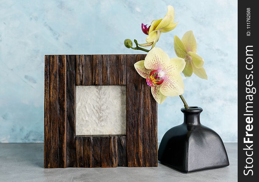 Wooden photoframe mockup with yellow orchid against light blue wall. Interior design concept. Text space