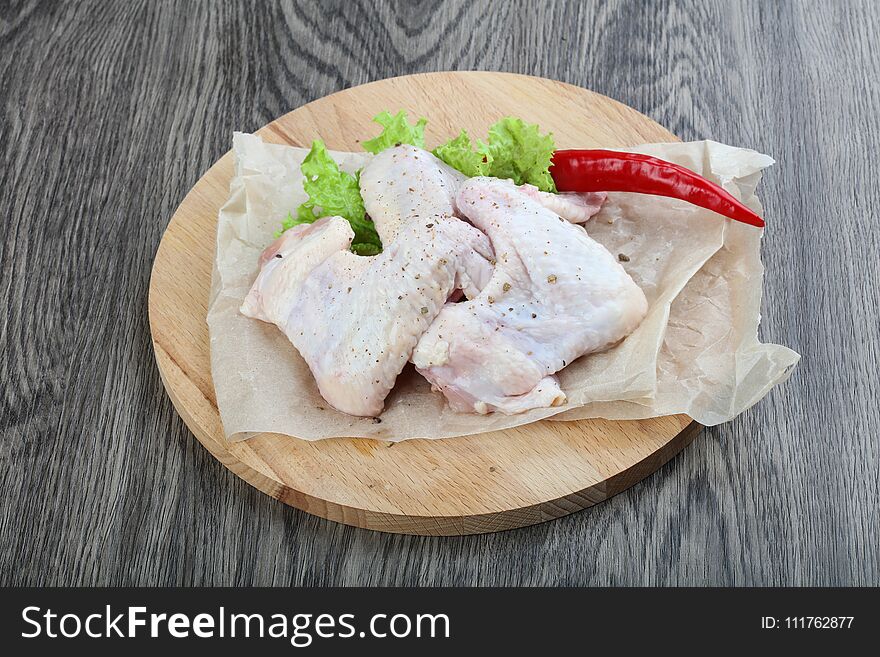 Raw chicken wings with salad leaves on wood background