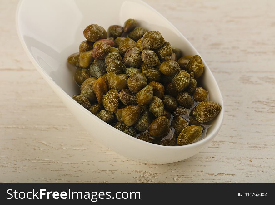 Marinated capers in the bowl over wood background. Marinated capers in the bowl over wood background