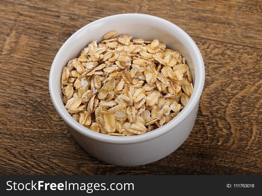 Raw oatmeal heap in the bowl over wooden background