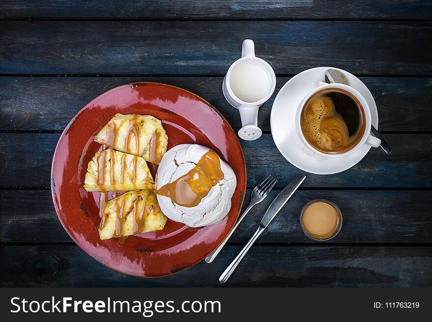 Delicious dessert. Meringue with pineapple and fresh coffee and milk on a colored wooden background. Top view