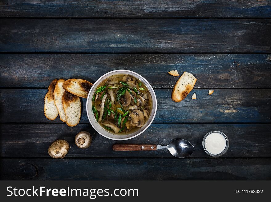 Fresh mushroom soup with green onion sour cream and bread crisps. In white bowl dishe. Colored wooden background, spoon. Top view. Fresh mushroom soup with green onion sour cream and bread crisps. In white bowl dishe. Colored wooden background, spoon. Top view.