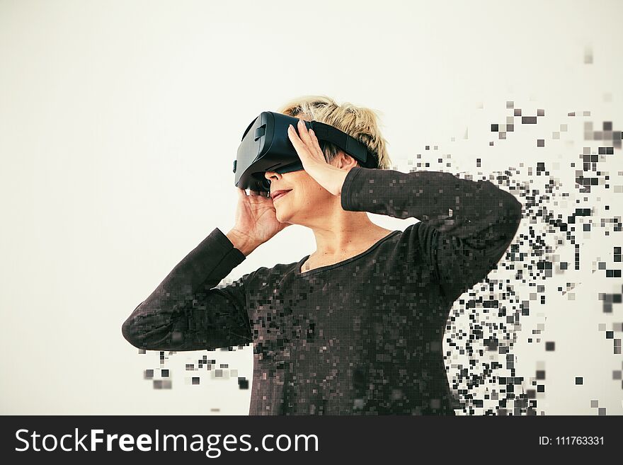 An elderly woman in virtual reality glasses is scattered by pixels. Conceptual photography with visual effects with an