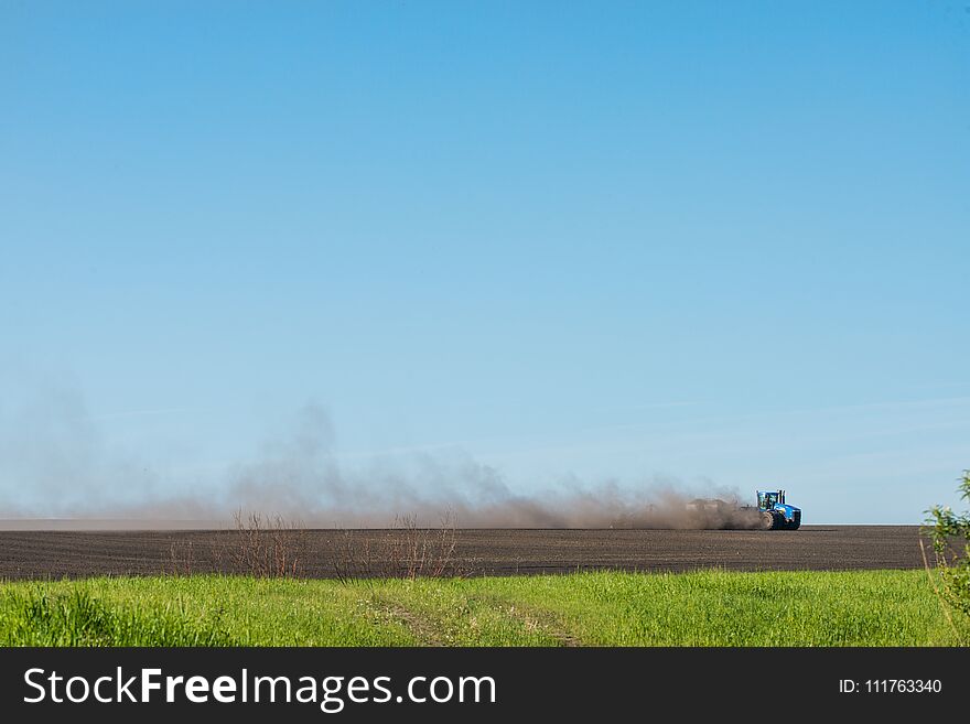 Blue tractor plowing field at sunny day