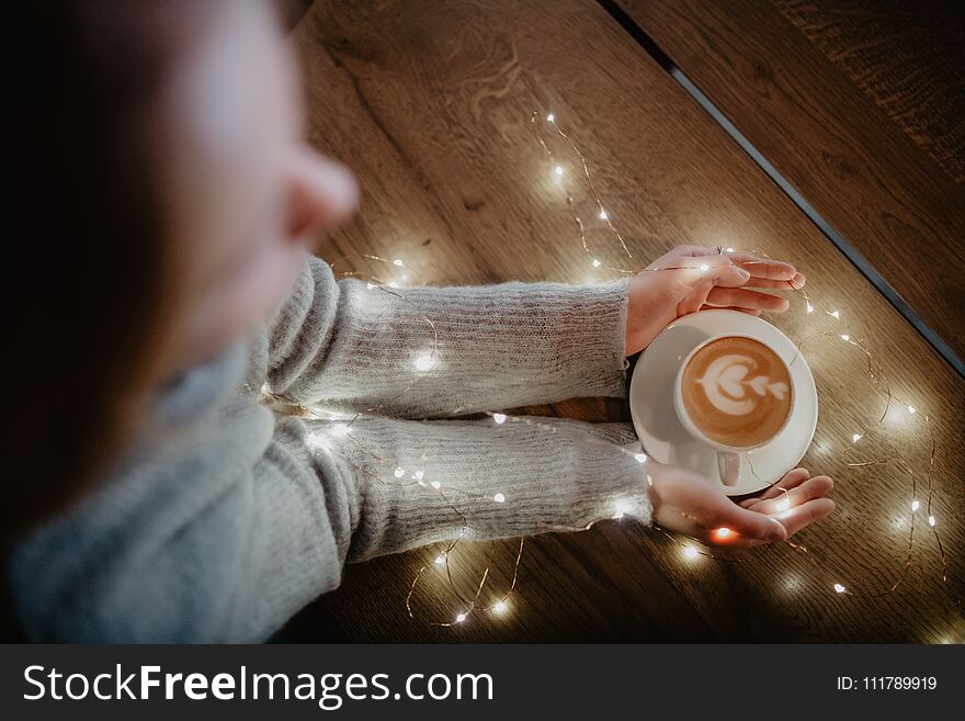 Girl holding coffee in hands over light bokeh background. Nice winter photo of hands with coffee cup with magic light.