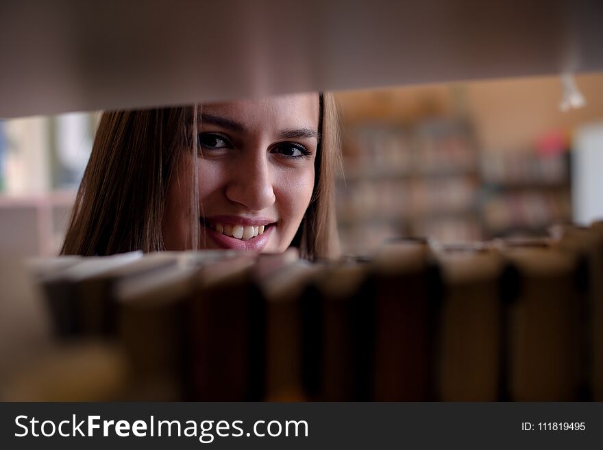 Young smiling woman looking through bookshelf. Young smiling woman looking through bookshelf.