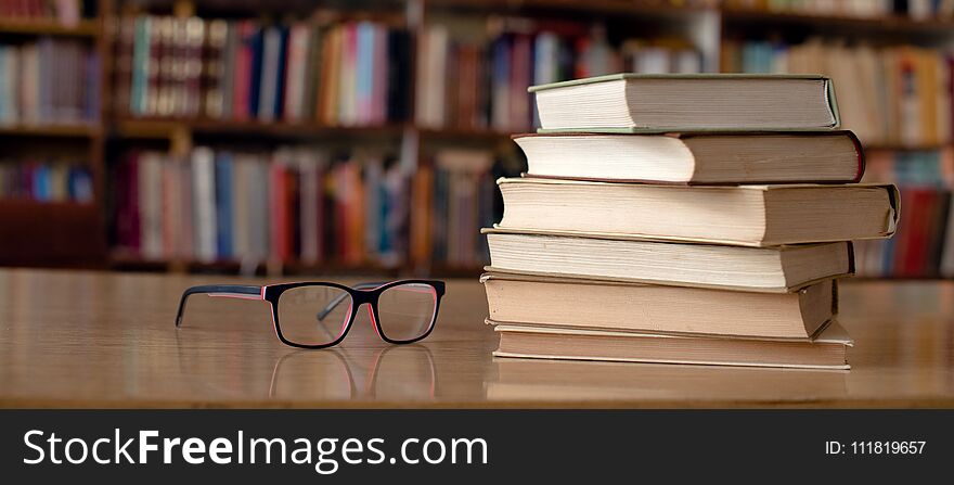 Books and eyeglasses on wooden desk in library. Books and eyeglasses on wooden desk in library.