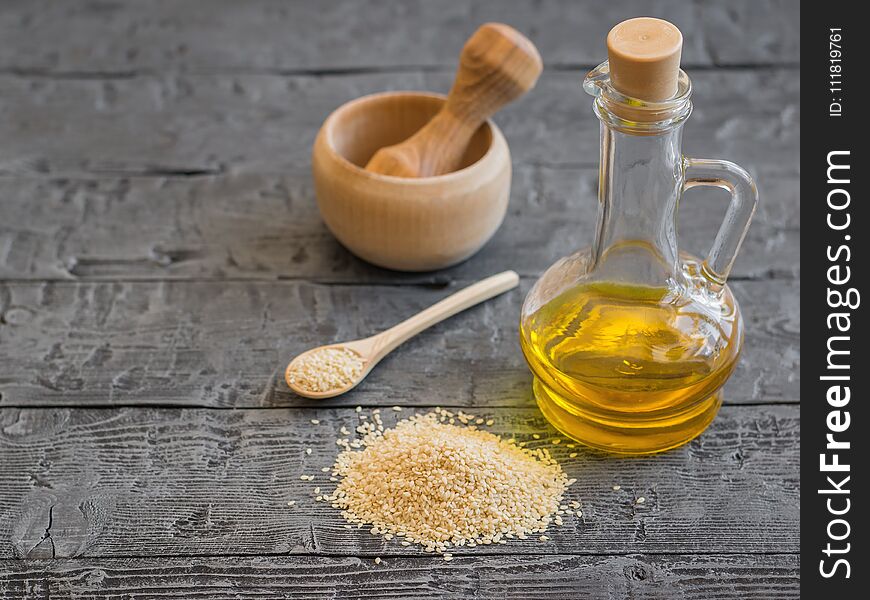 Sesame seeds, oil bottle and mortar with pestle on dark wooden table. Natural vegetarian food.