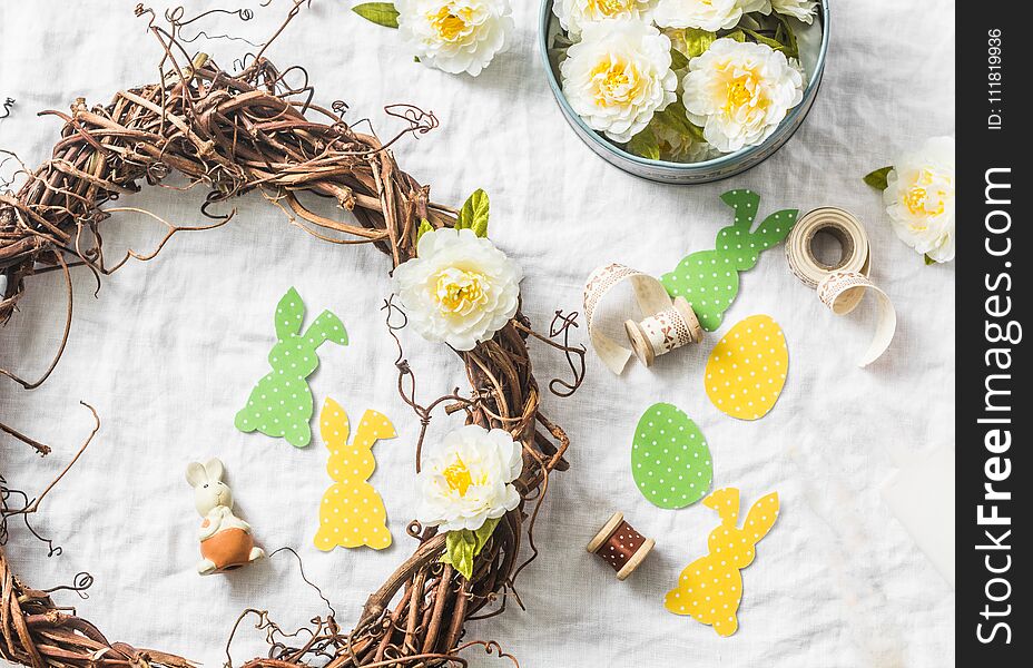 Homemade Easter wreath of vines with flowers, paper rabbits, ribbons on a white background, top view. Easter craft decorations hom