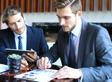 Two Young Businessmen Analyzing Financial Document At Meeting. Royalty Free Stock Image