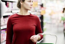 Young Woman With Shopping Cart In Supermarket. The Girl In The Background Of The Store Looks At The Goods. Shopping Concept Royalty Free Stock Photo