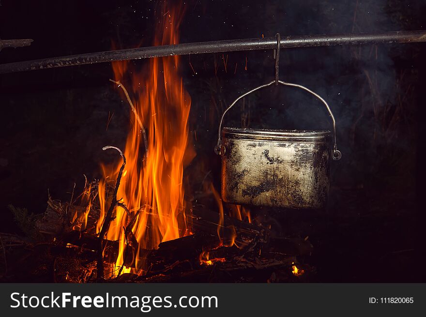 Boiling water in the bowler on the bonfire. Hiking romance around the campfire at night.