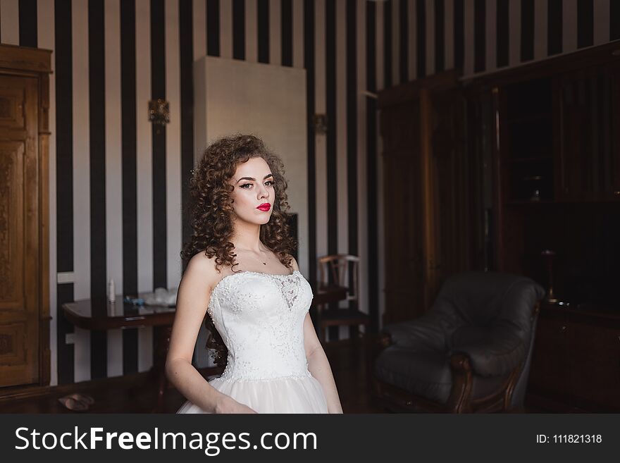 A beautiful bride is standing in a room by the window her hair is curly