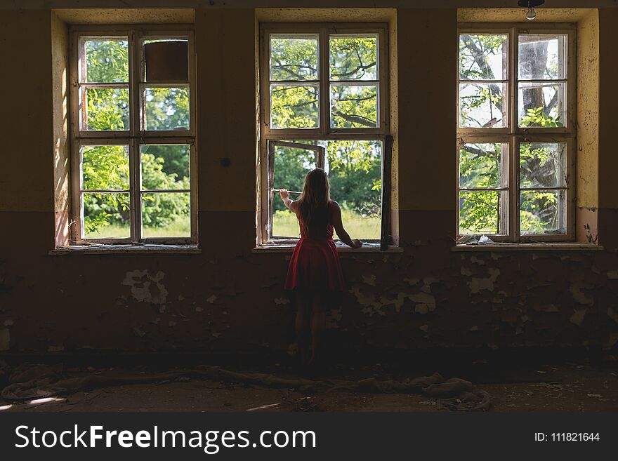 Woman in red dress looking through the window in the old building at summer sunny day