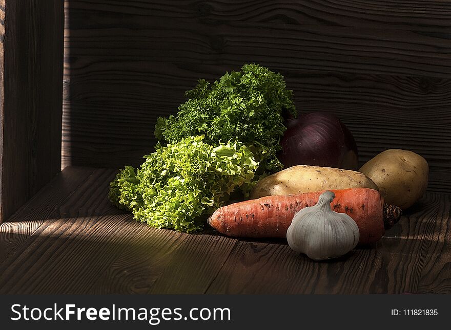 Greens and root crops on a dark rustic table, lit by oblique rays