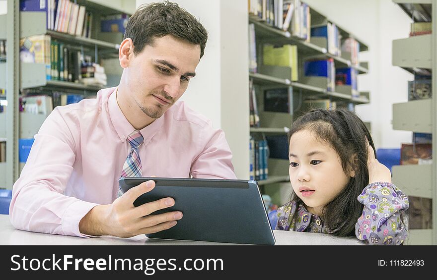 man teacher and kid student learning and looking on tablet device with self book in the background