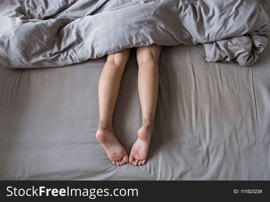 Close Up Of Barefoot And Leg Under Blanket On The Bed