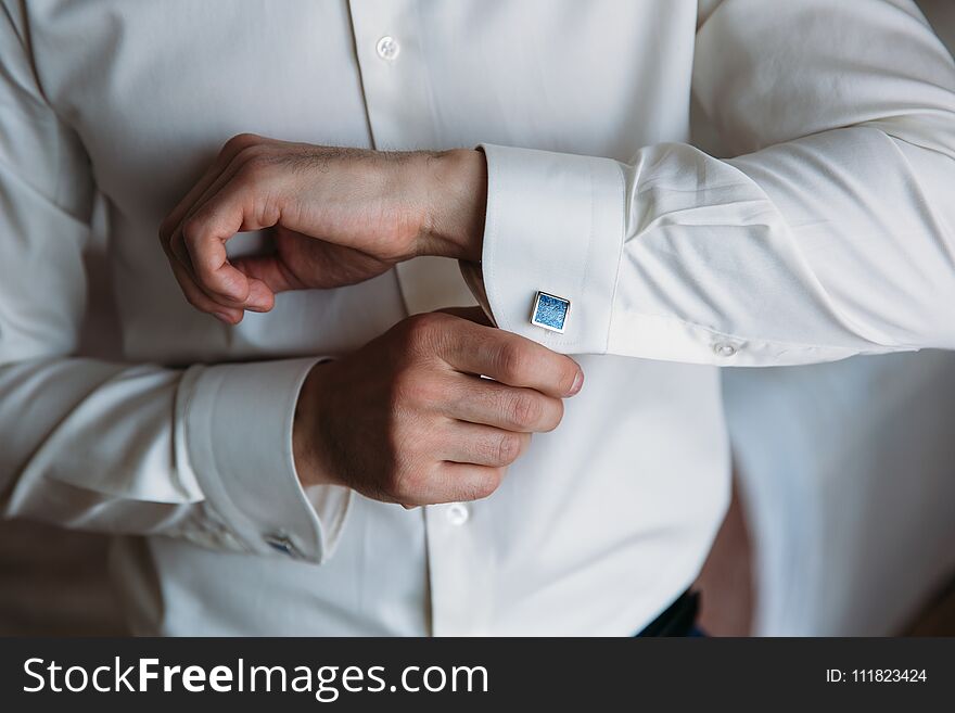 Groom hands hold cufflinks. Elegant gentleman clother, white shirt and black belt.