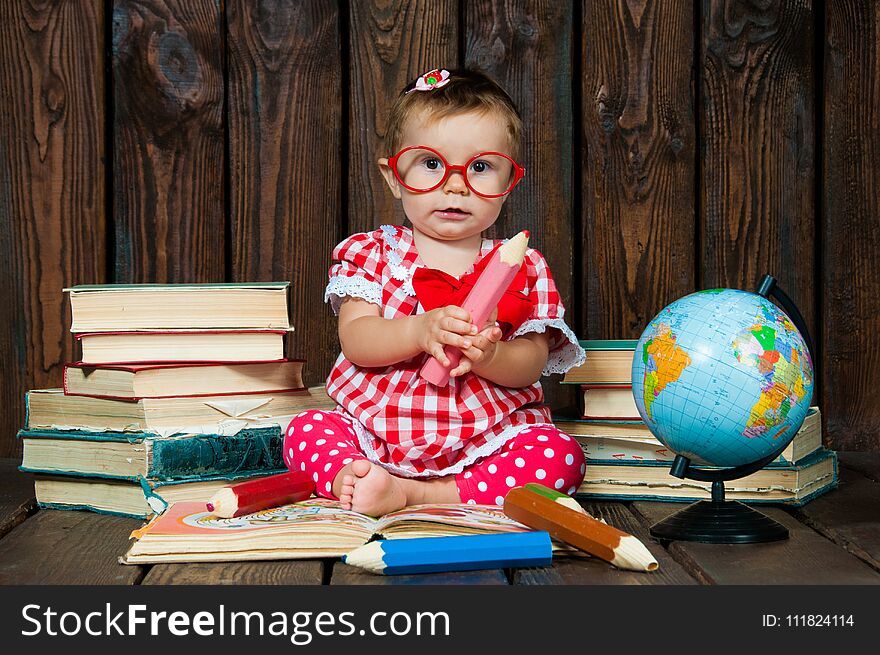 Happy a nice little girl with glasses and pencils against the background of books and a globe.