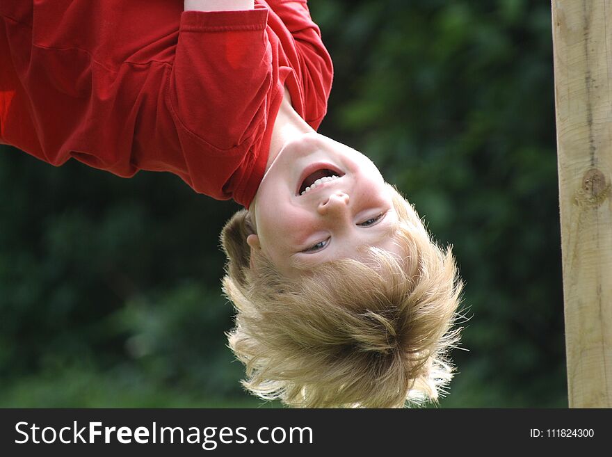 A happy laughing boy hanging upside down in a children`s playground. A happy laughing boy hanging upside down in a children`s playground.
