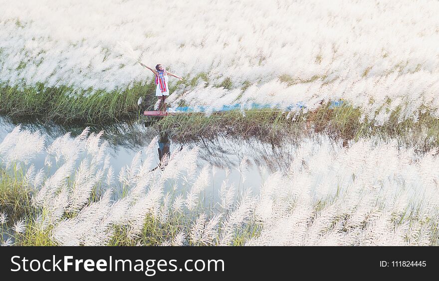 Portrait of beautiful Asian woman standing on fishing boat, enjoy natural outdoor at lake with grass flower at sunset