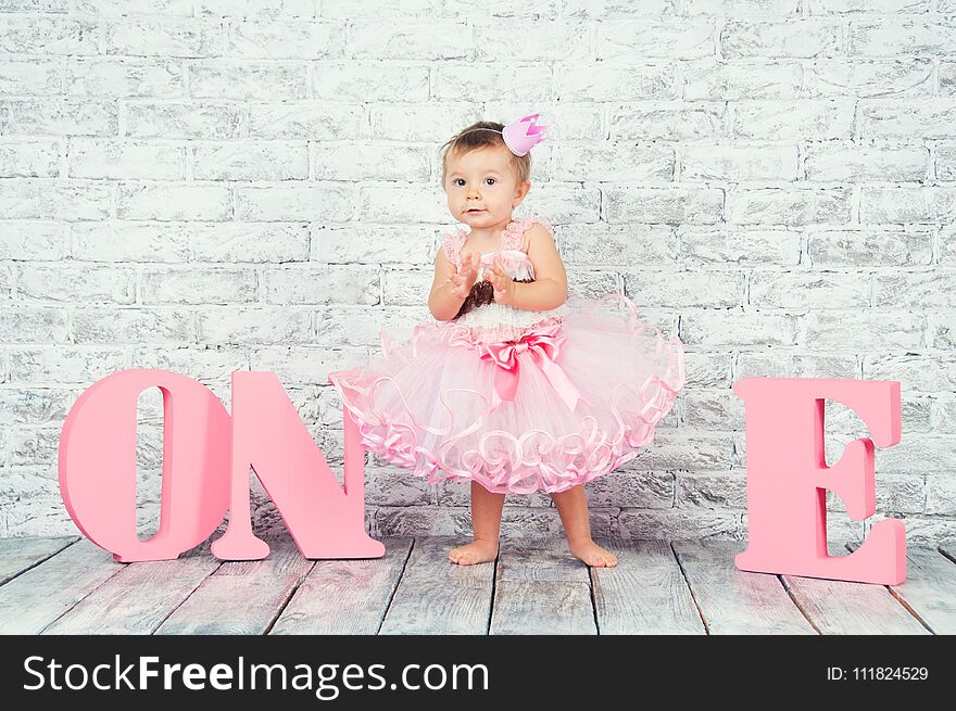 Beautiful and cute girl in a pink dress with the letters one on her first birthday. Emotional girl.