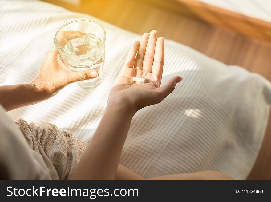 Woman With Pills Or Capsules On Hand And A Glass Of Water