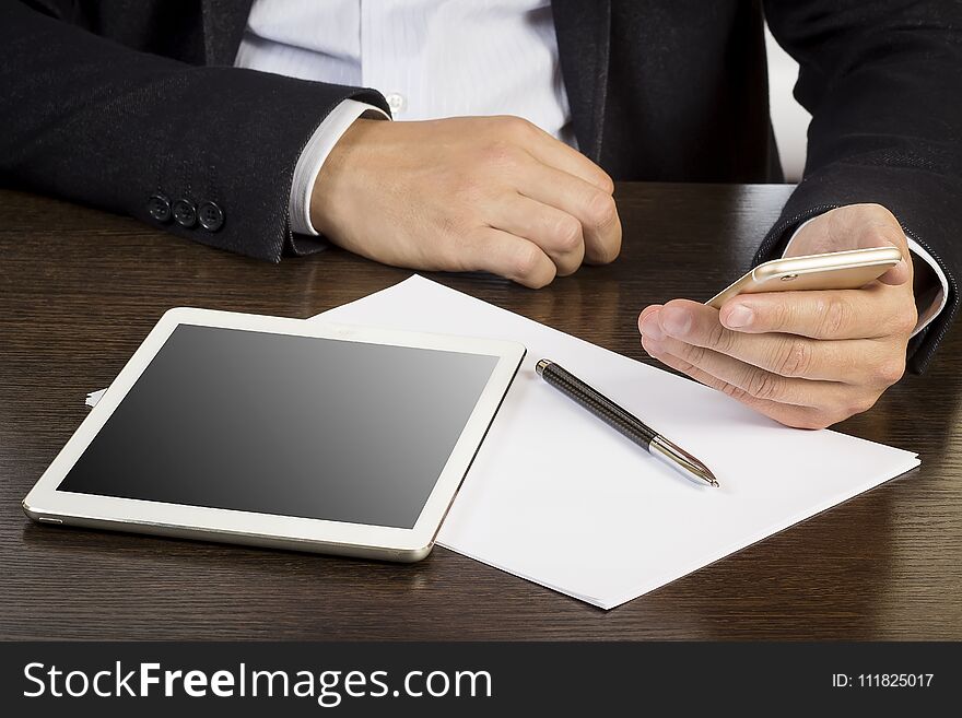 Hands of man in business suit on the desk with papers and electronic devices. Businessman uses smartphone at his desk in the office of the company