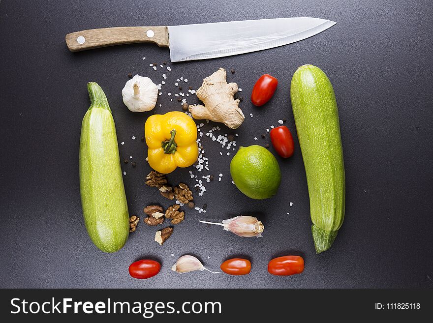 Vegetables And Knife On Black Ceramic Table. Ingredients For Cooking. Zucchini, Peppers, Tomatoes, Garlic, Lime, Nuts And Salt