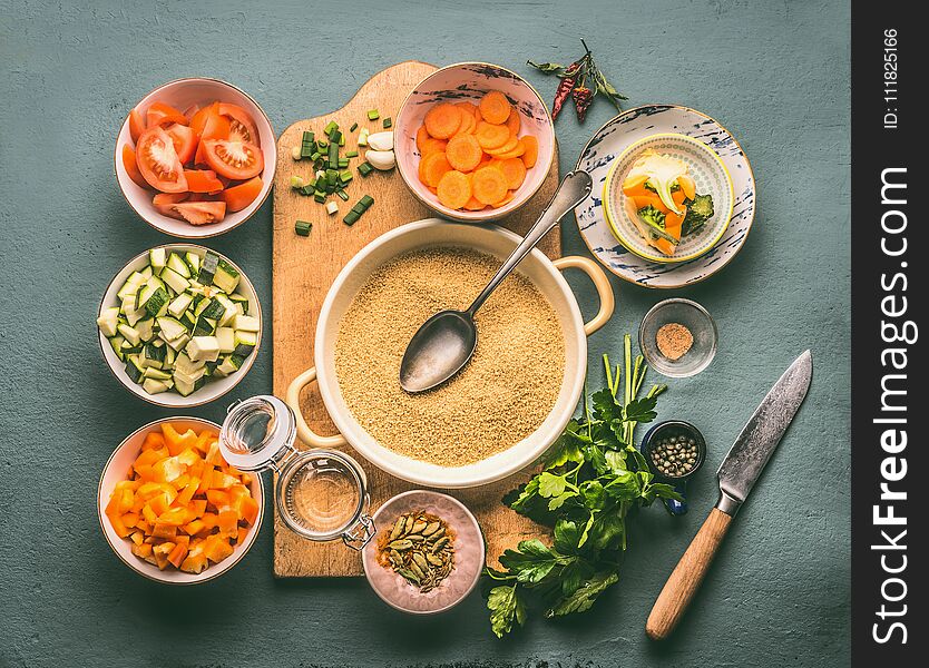 Couscous and vegetarian cooking ingredients in bowls on cutting board with spoon , gray background