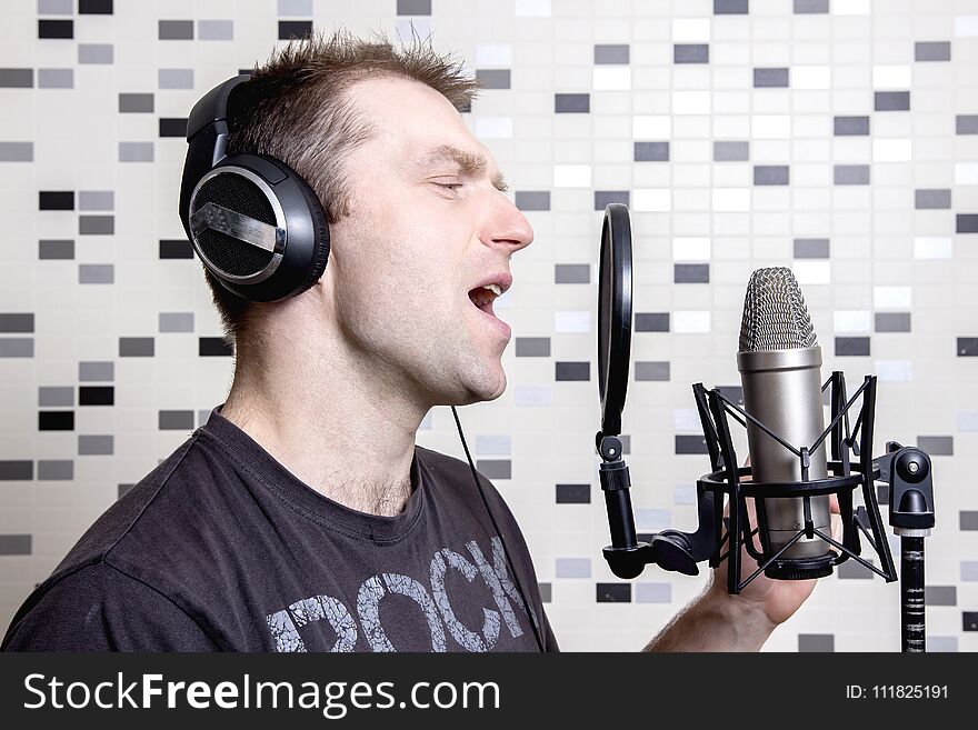 A young guy singer and rock musician sings in a studio condenser microphone in headphones in a recording studio. Record voice to microphone. Vocal is a rock musician.