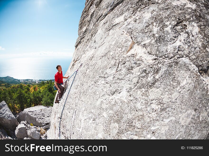 A rock climber on a rock. A man climbs the rock against the background of the sea coast. Active lifestyle. Sports in nature. Overcoming a difficult climbing route.