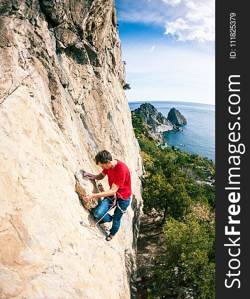 A rock climber on a rock. A man climbs the rock against the background of the sea coast. Active lifestyle. Sports in nature. Overcoming a difficult climbing route.