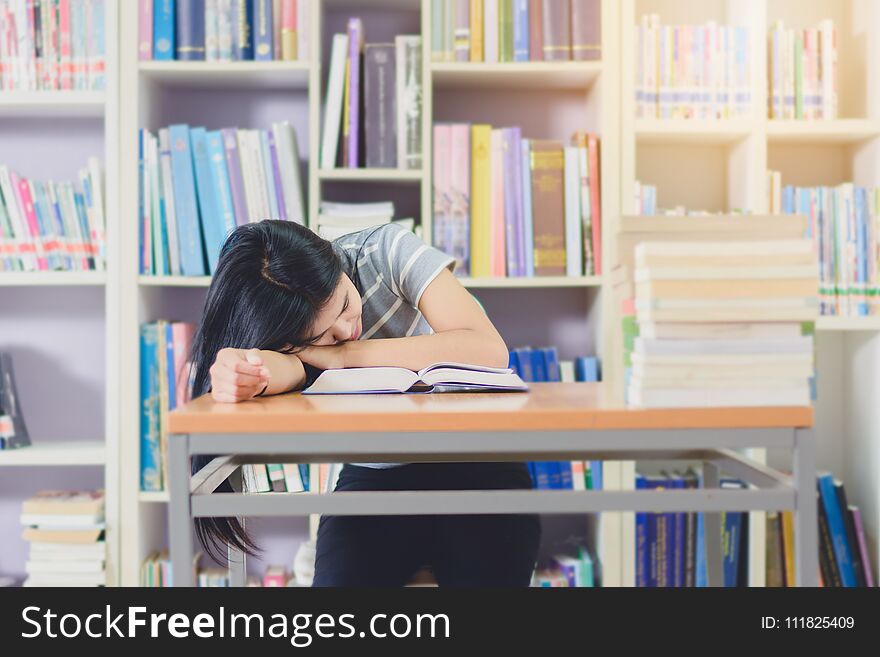Portrait of clever Asian student exhausted for reading and doing research in college library