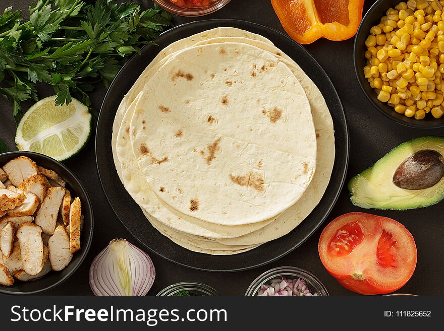 Tacos ingredients background with flatbread, fresh vegetables and roasted chicken meat on the table. Mexican fast food top view with copy space.