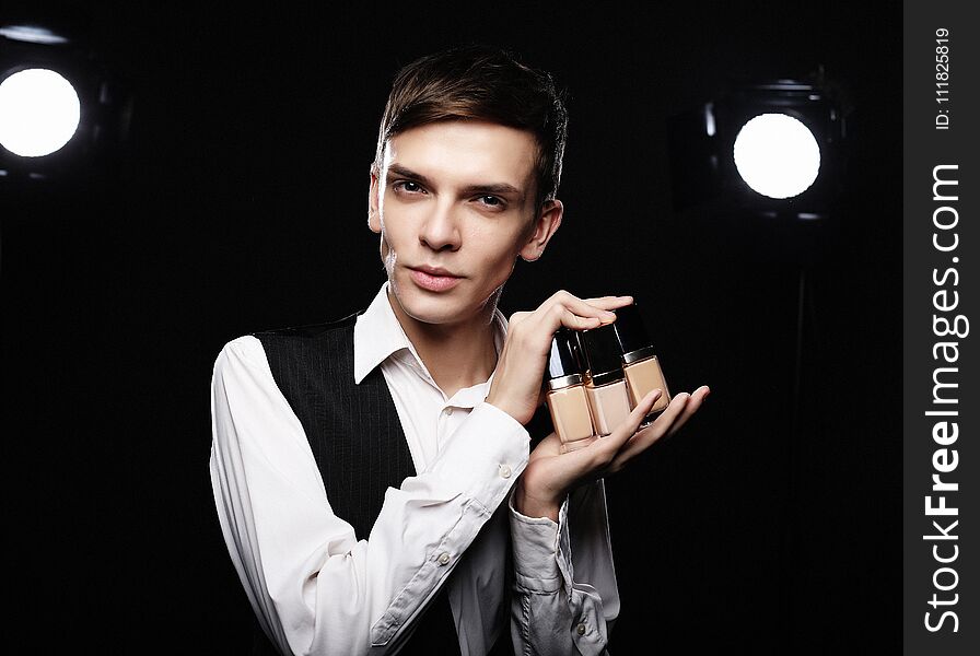 Beauty concept. Young male make up artist posing with foundation for make-up on a dark background.
