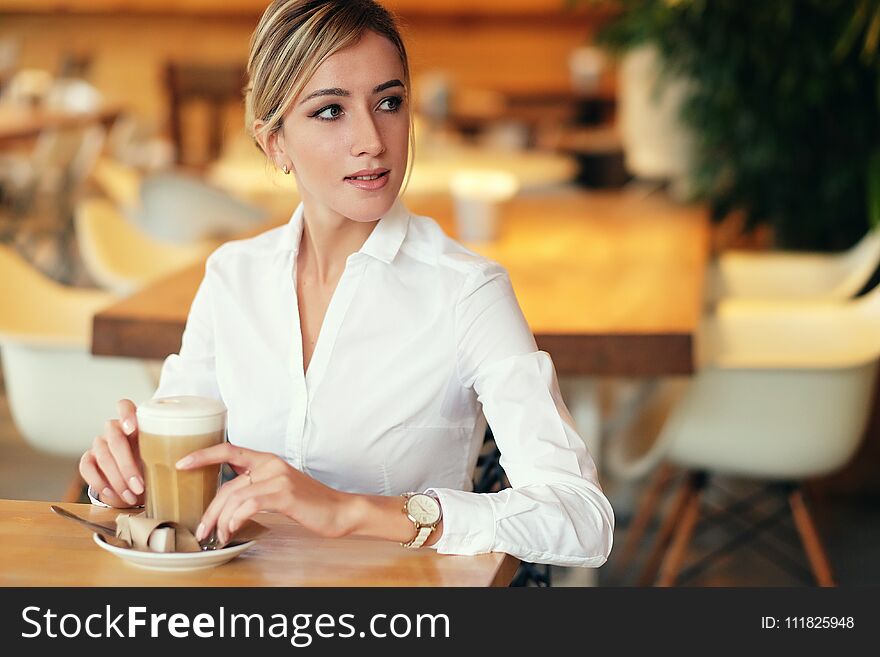 Smiling young woman in a good mood with cup of coffee sitting in cafe. Bright sunny morning. Smiling young woman in a good mood with cup of coffee sitting in cafe. Bright sunny morning