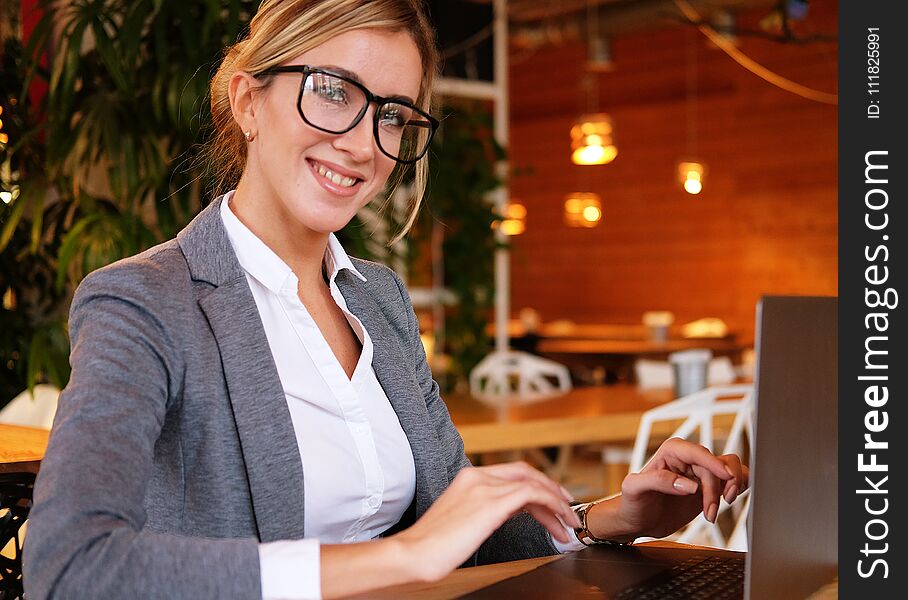 Business wooman using laptop at cafe. Young beautiful girl sitting in a coffee shop and working on computer. Lifestyle and business concept.